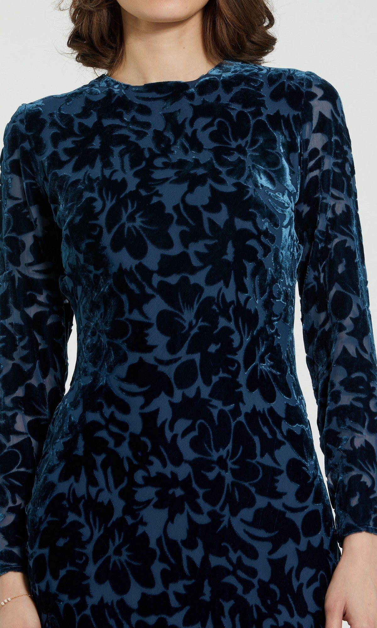 A woman wearing the Midi Party Dress: Mac Duggal 81129—a long-sleeved, dark blue burnout velvet midi dress with a bold floral pattern—shown from shoulders to above the waist.
